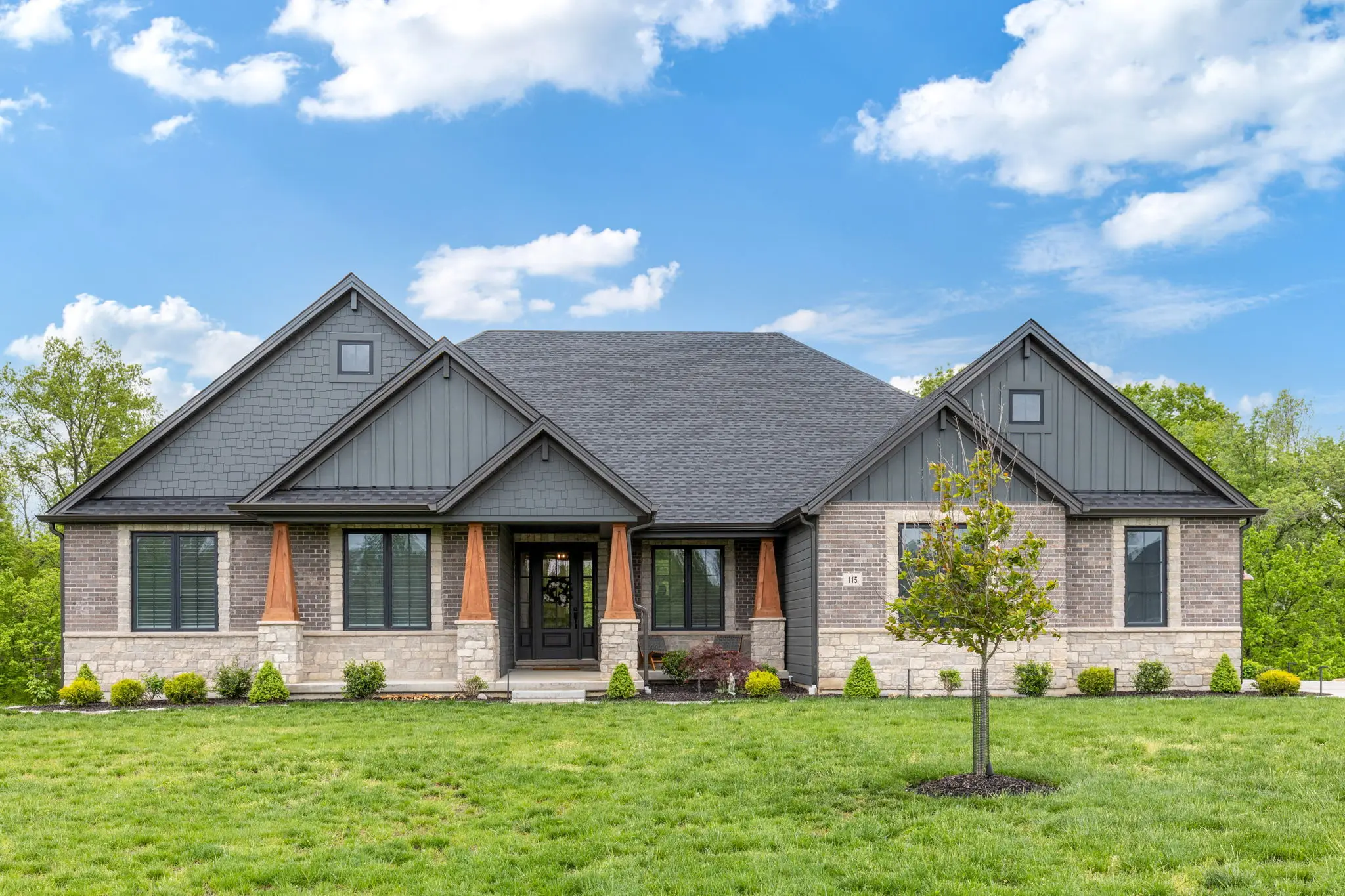 Craftsman home with stone-and-shake gables, brick base, and a manicured front lawn.